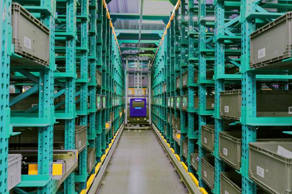 Aisle between tall green storage racks holding totes